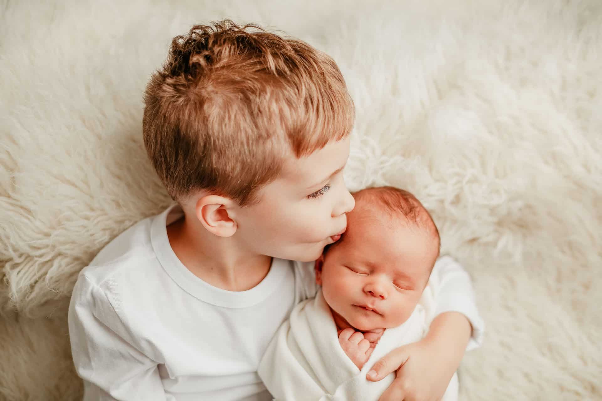 Big brother kissing baby brother in newborn photo session
