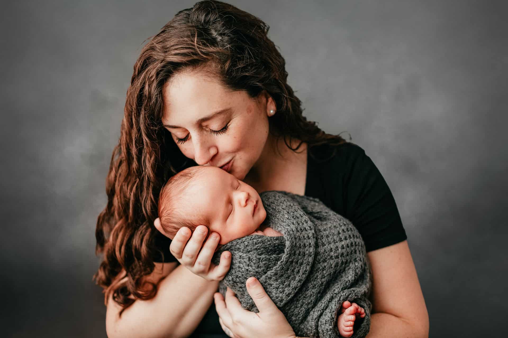 Mom kissing sleepy newborn baby in studio portrait image