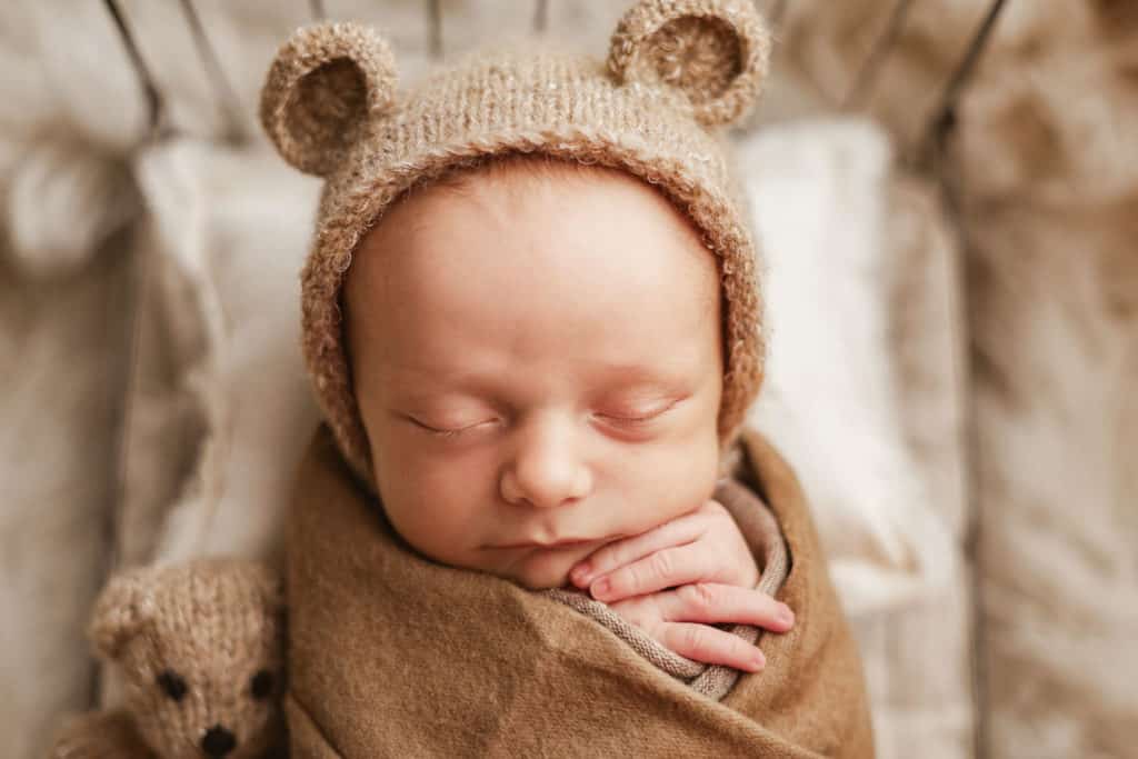 newborn baby boy in bear bonnet with brown wrap on tiny prop bed
