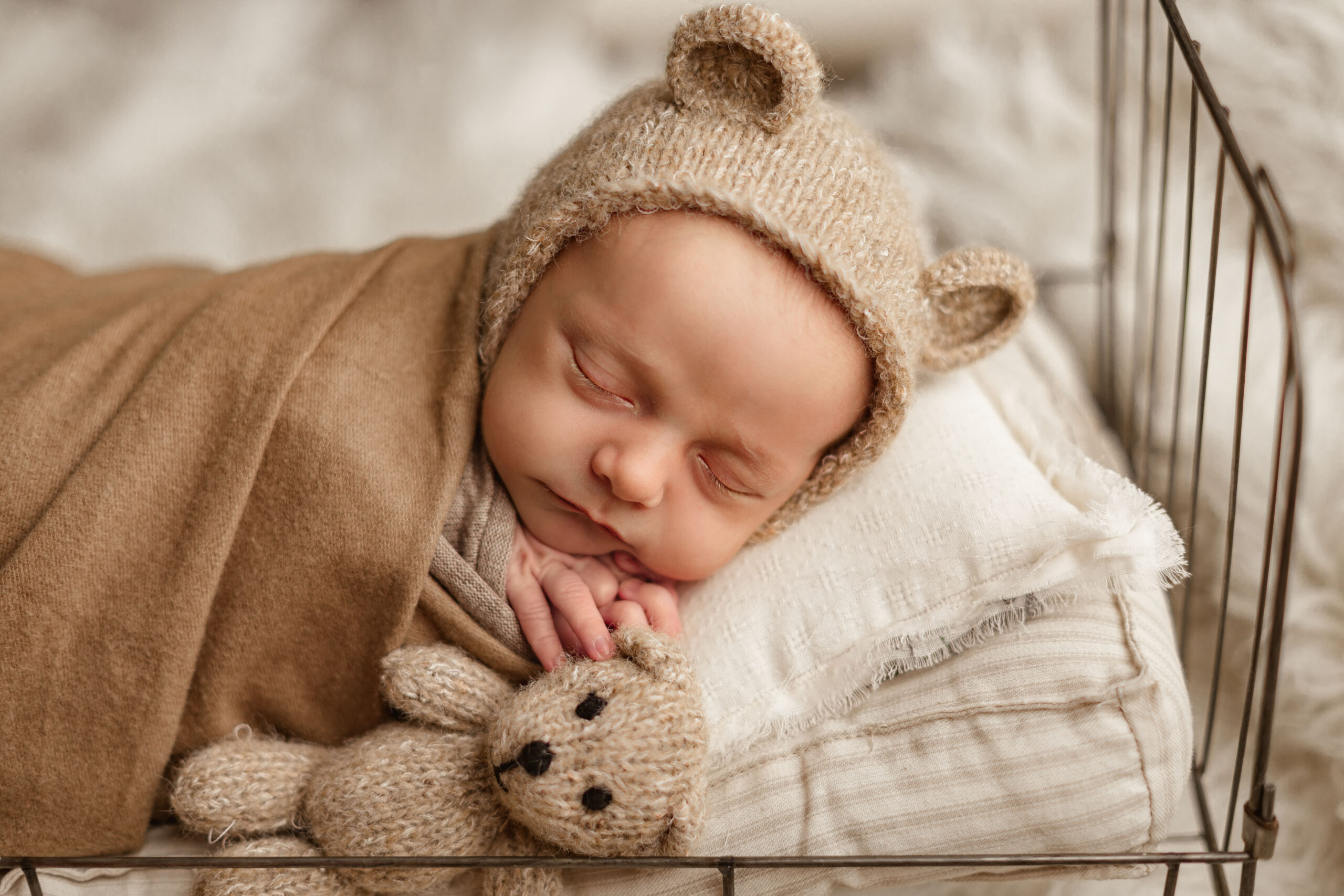 newborn baby wrapped in brown wearing a bear hat sleeping on a bed Nashville baby boutiques