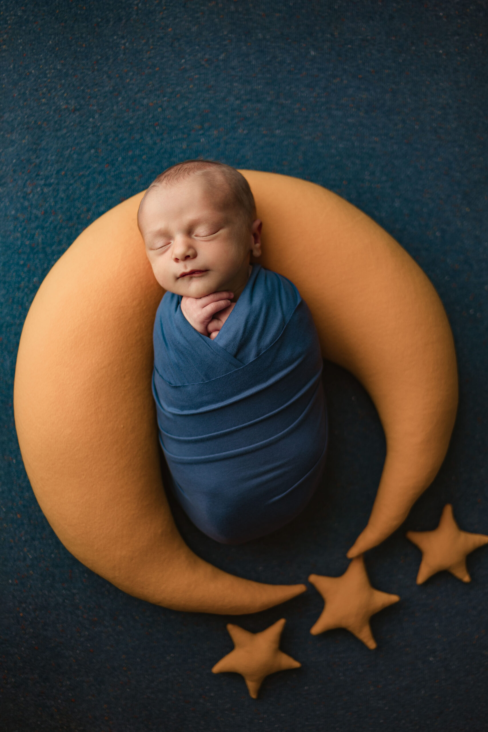 newborn baby wrapped in blue laying on a gold moon pillow