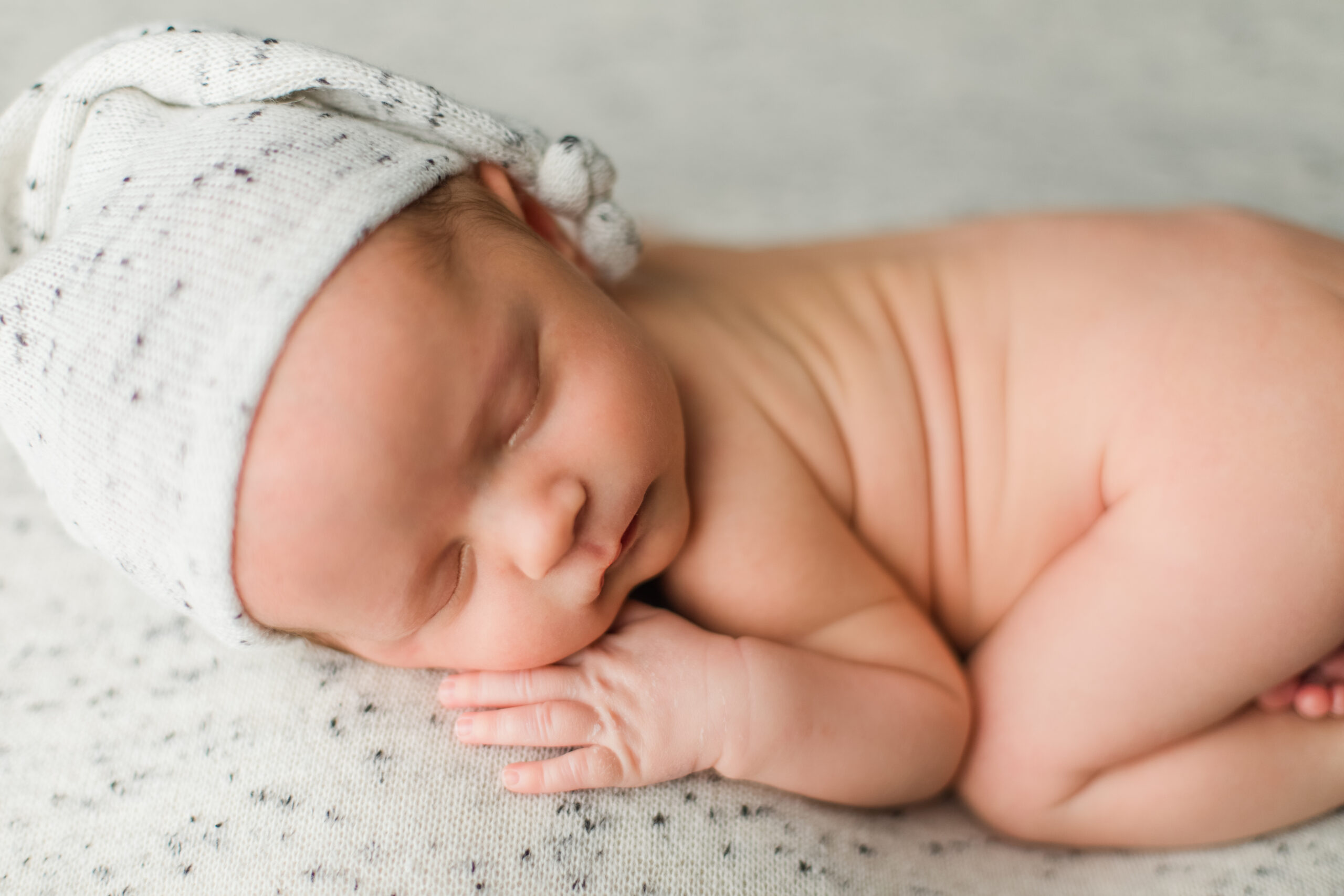 newborn baby sleeping on a white blanket with a night cap nashville lactation consultant