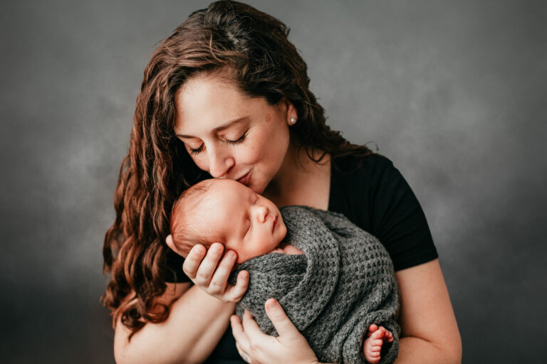new mom holding her newborn in a studio and kissing them on the head