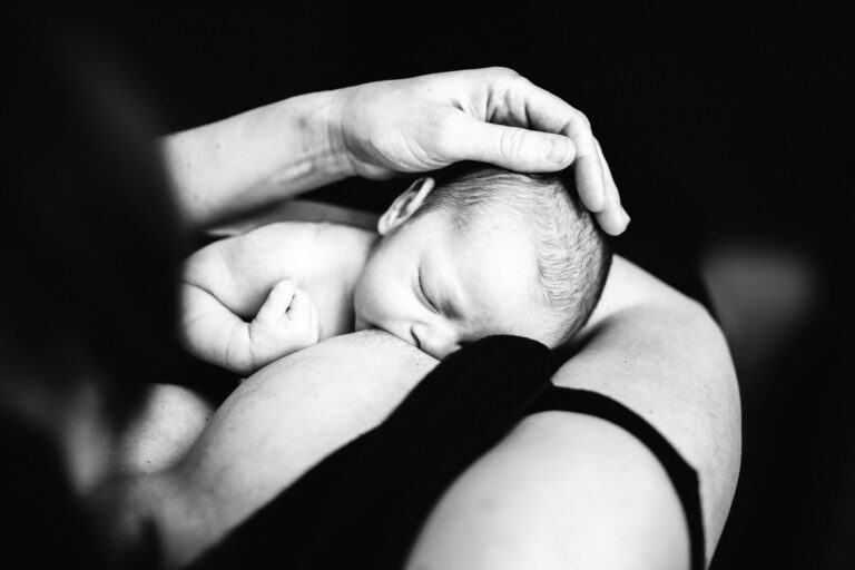 newborn breastfeeding while mom touches her head