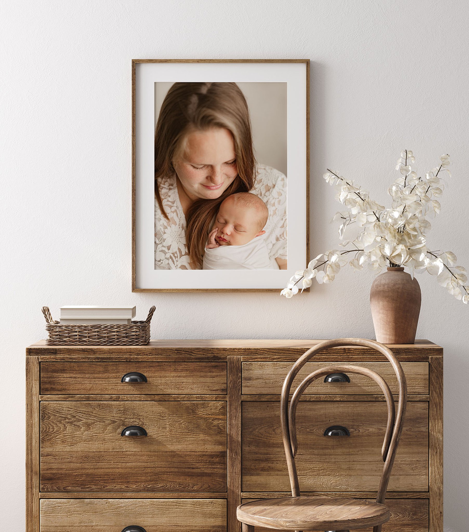 Artwork of a mom holding her sleeping newborn hangs above wooden drawers