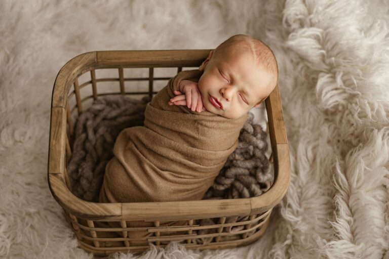 Newborn baby sleeps swaddled in a brown blanket in a wooden basket Nashville interior designers