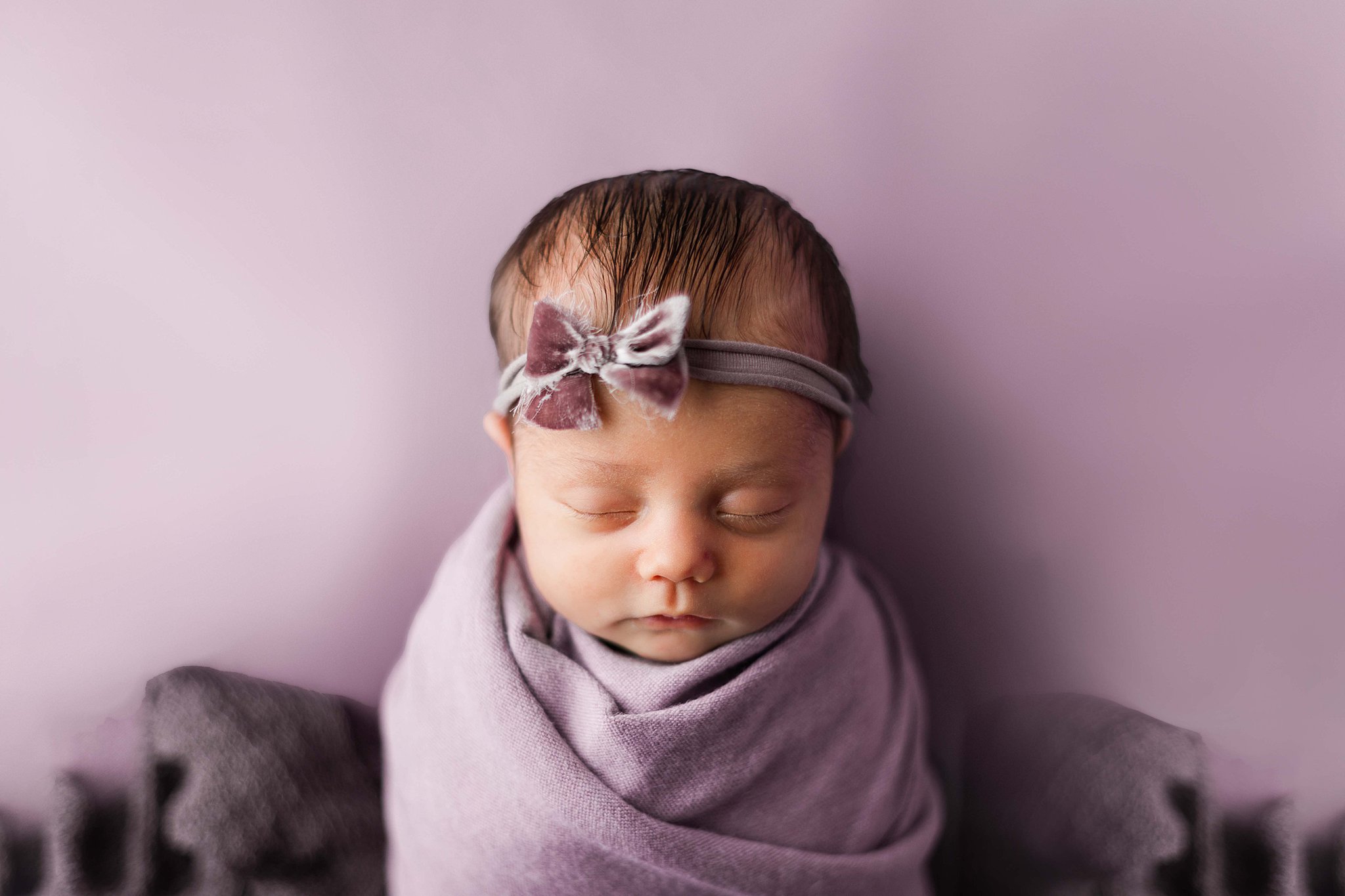 baby sleeps in a purple swaddle and purple bow