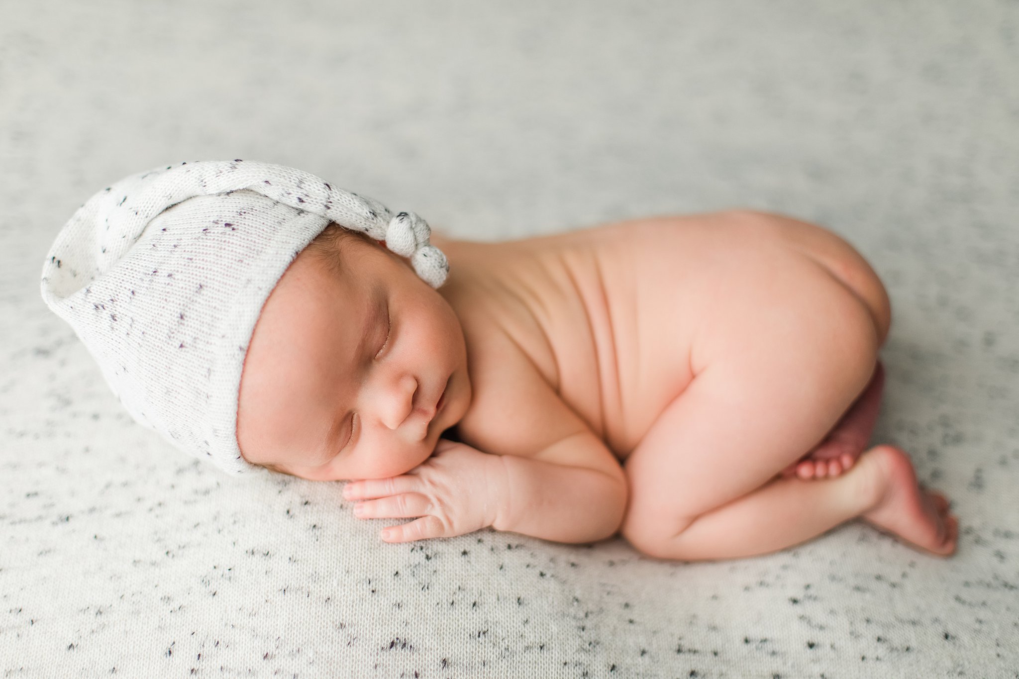 A newborn baby in a speckled hat sleeps in froggy pose on a matching blanket Tennessee Maternal Fetal Medicine