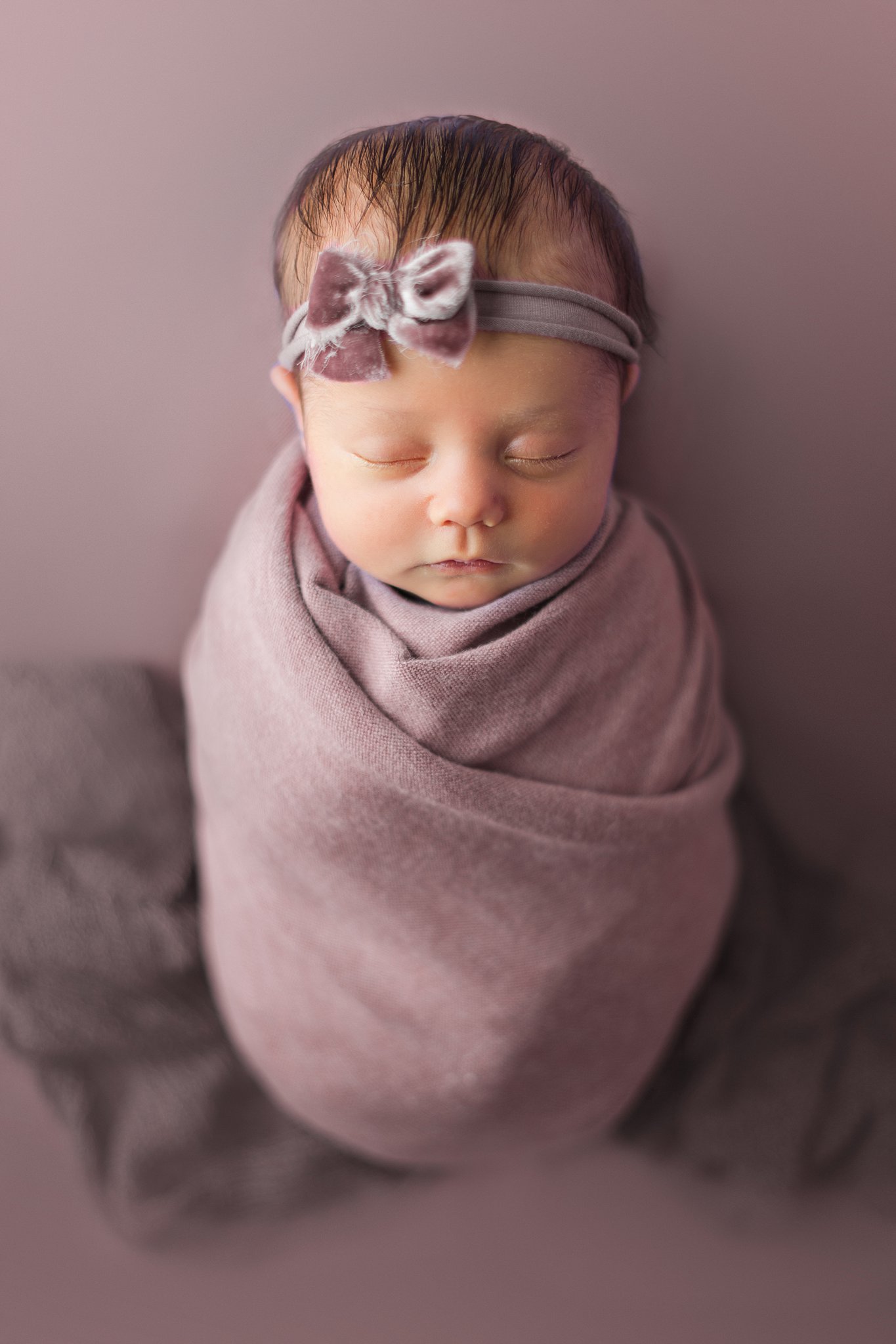 A swaddled newborn baby sleeps in a purple blanket