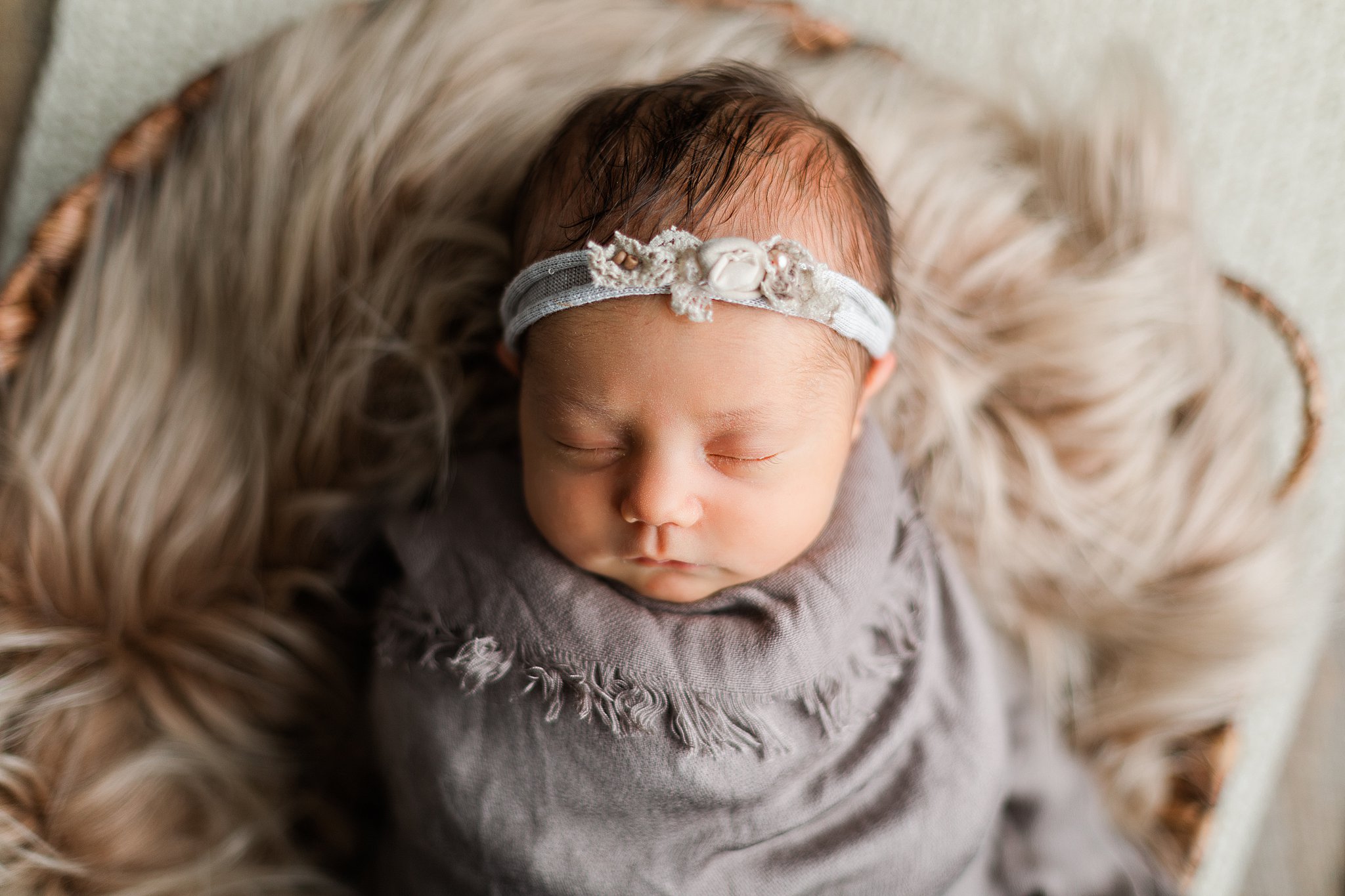 Newborn baby sleeps in a wicker basket wearing a headband wild child boutique
