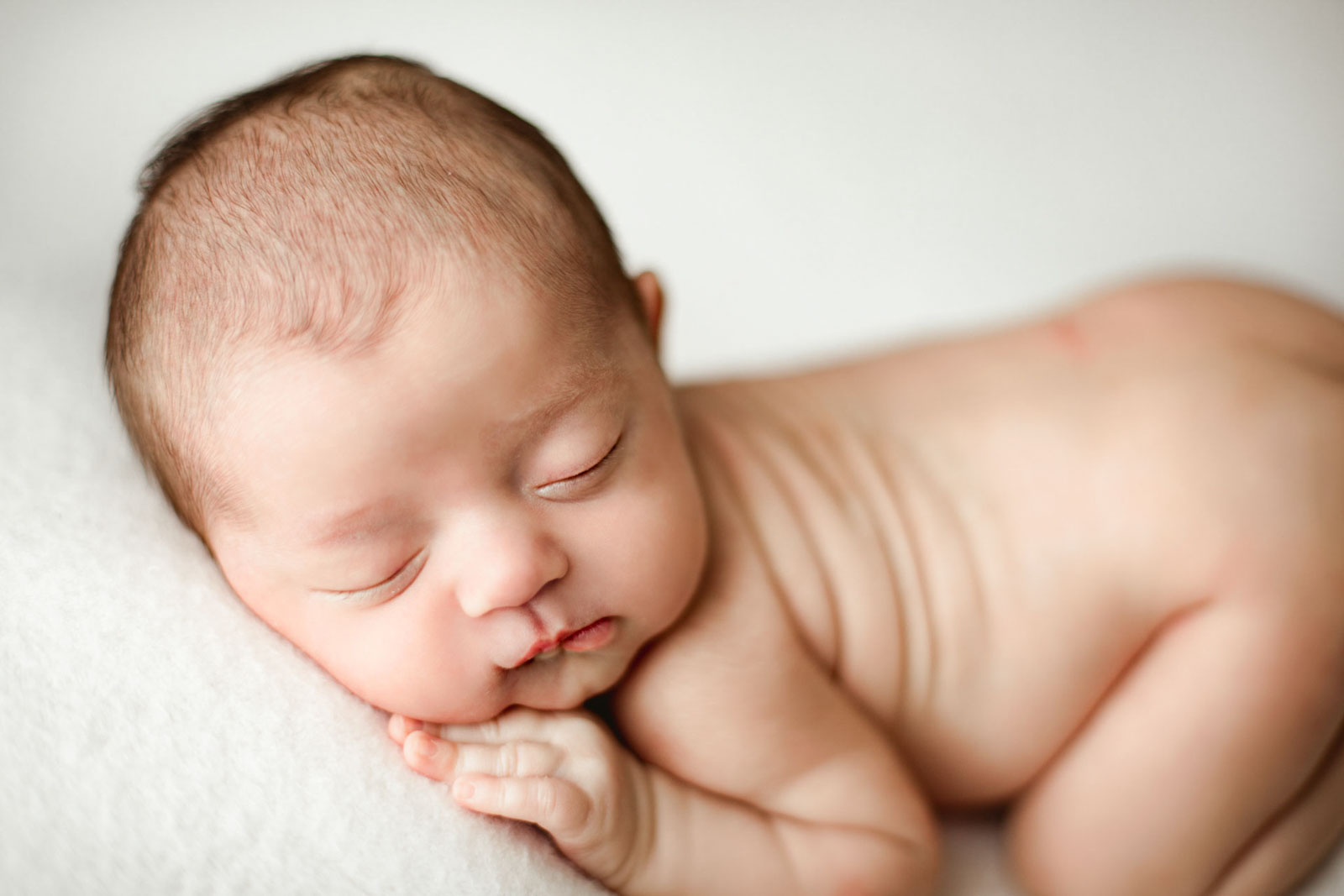 newborn baby posed on cream white background. sleepy baby with hand under cheek.