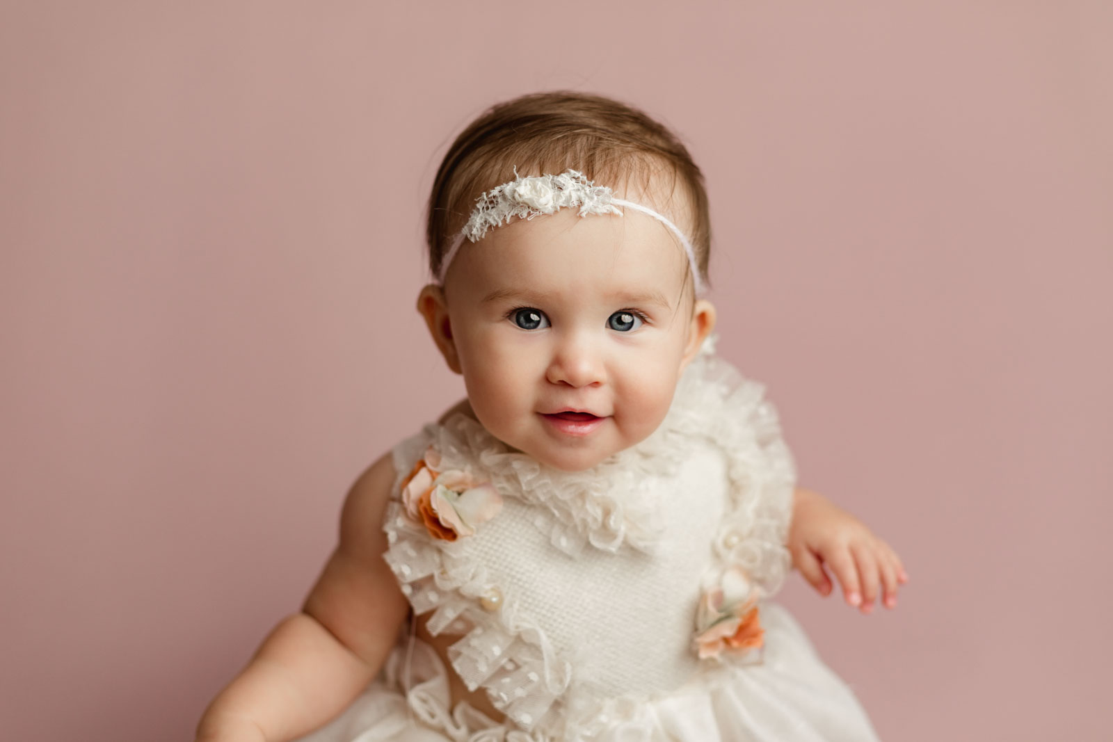 small baby girl sitting with smile, wearing a cream dress with heart shaped top