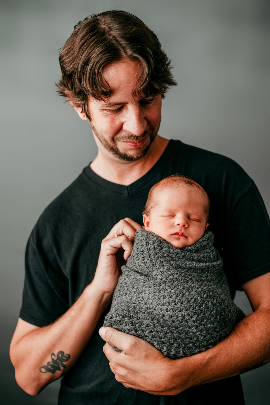 A father in a black shirt looks down on and holds his newborn child in a studio patch nashville