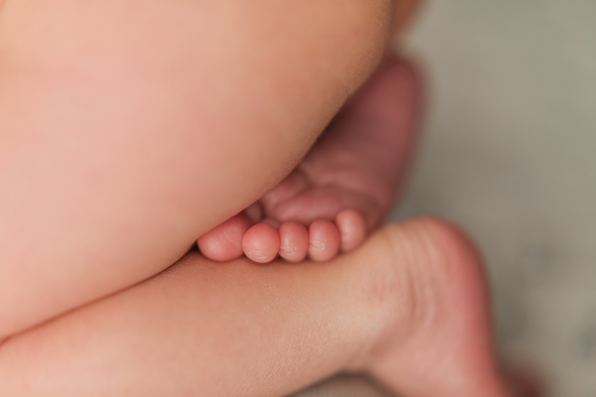 A newborn baby foot rests on the opposite ankle with toes curled