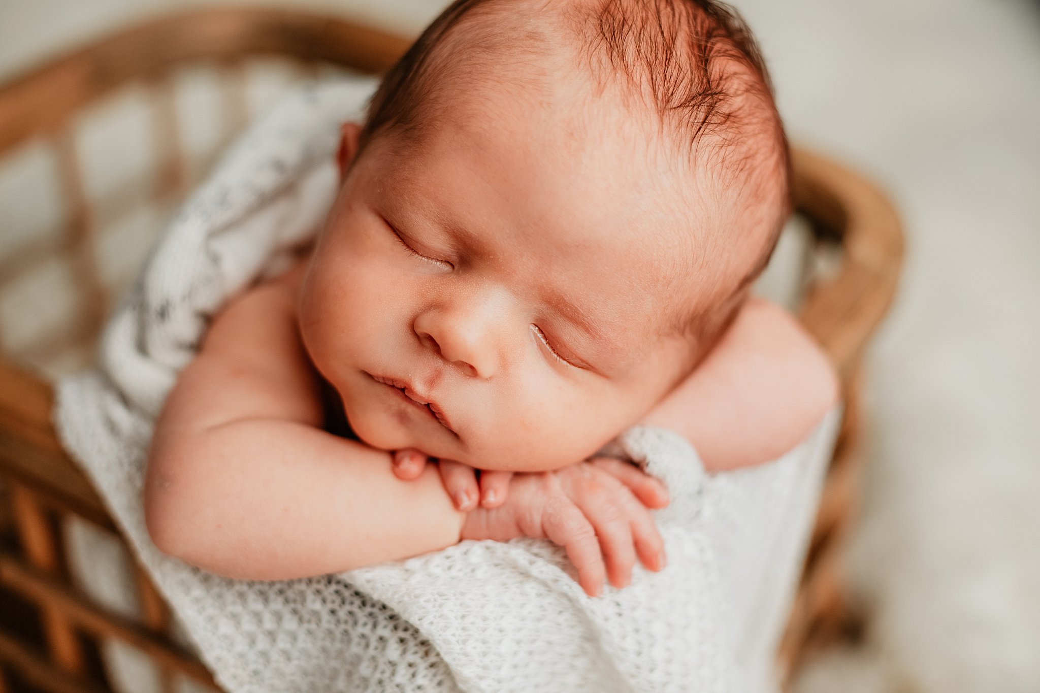 A newborn many sleeps in a wooden basket with head resting on it's hands vanderbilt birth center